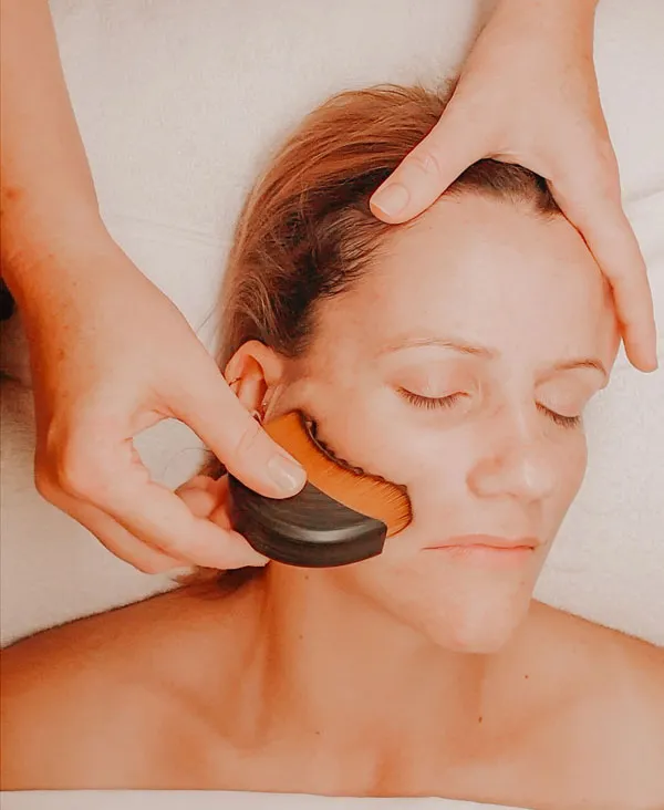 Bec using brush tools to massage her client during a TMJ massage facial